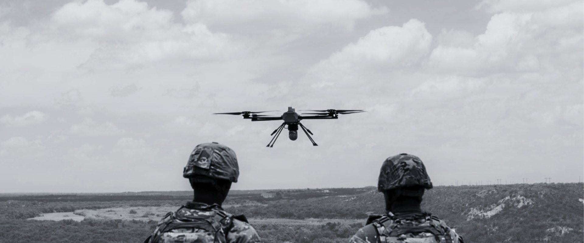 Two soldiers watching a small drone hover above a river valley