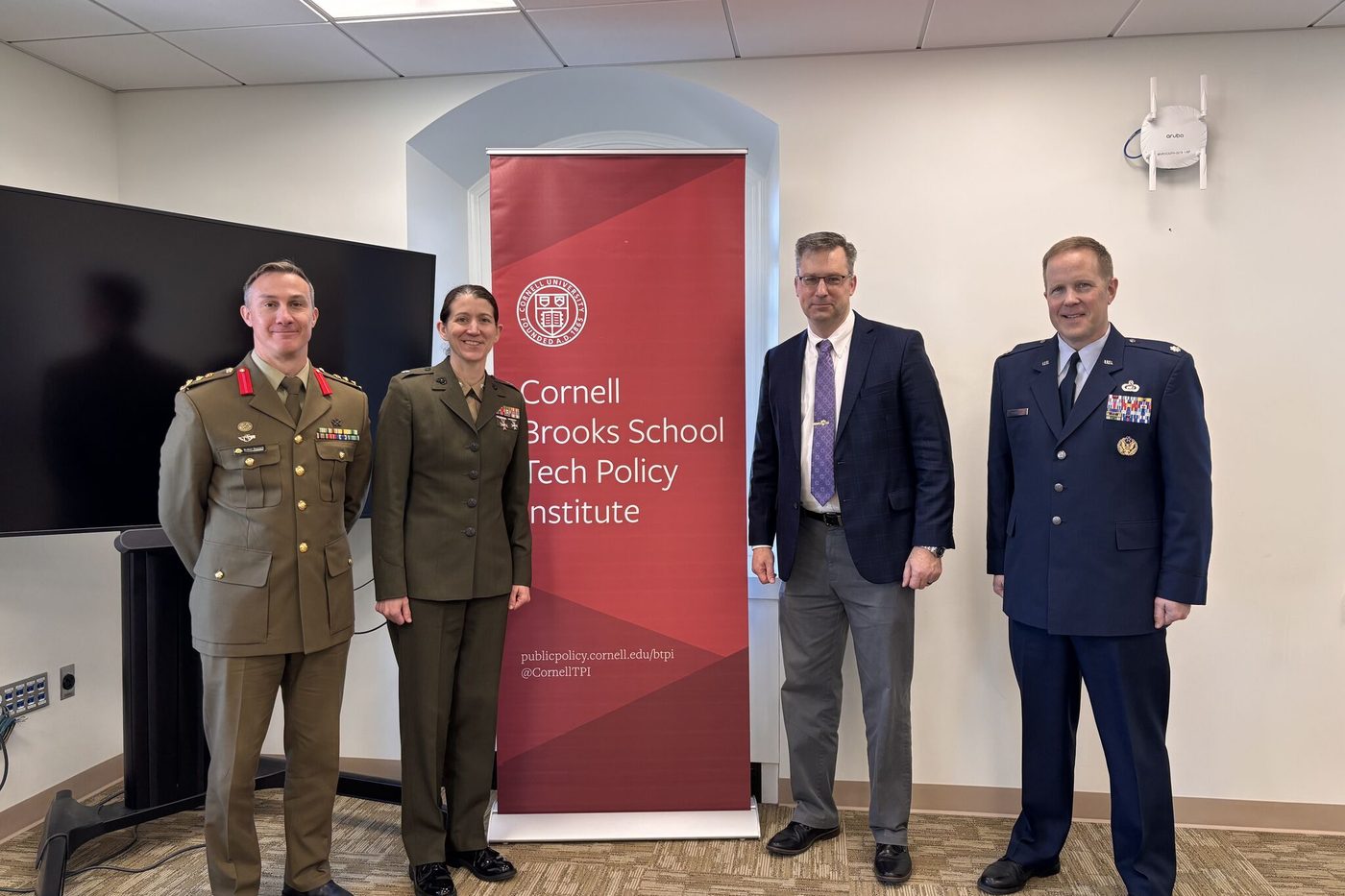 Four officers in the uniforms of several nations standing beside a Tech Policy Institute banner