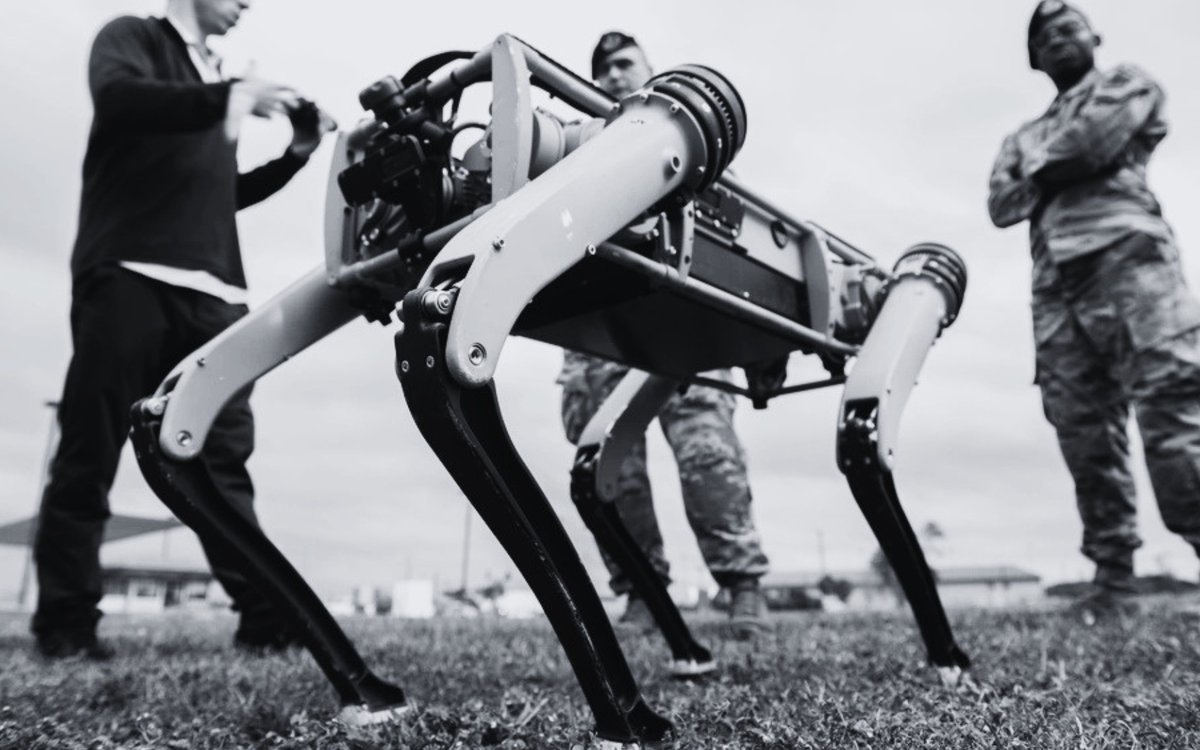 Airmen observing a four-legged unmanned ground vehicle walking on grass